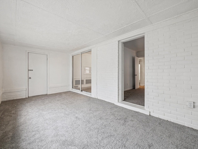 empty room featuring a textured ceiling, brick wall, and carpet flooring