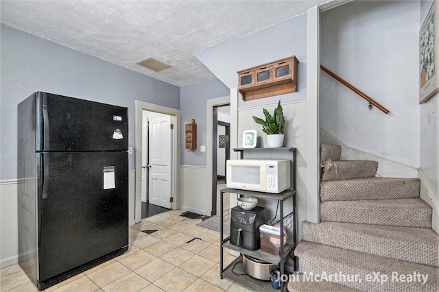 kitchen featuring white microwave, visible vents, light tile patterned floors, freestanding refrigerator, and a textured ceiling