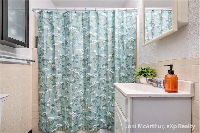 full bathroom with vanity, tile walls, curtained shower, and a textured wall