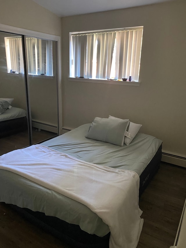 bedroom with dark wood-type flooring, multiple windows, and a baseboard heating unit