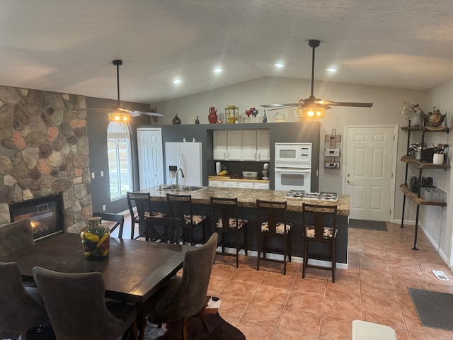 tiled dining room with ceiling fan, sink, a fireplace, and vaulted ceiling