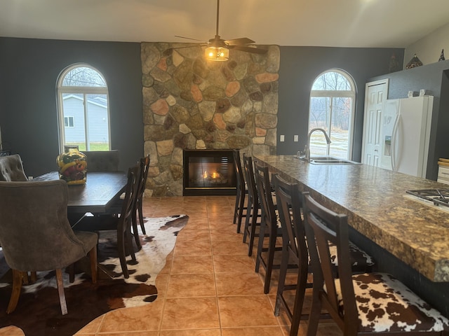 dining area featuring light tile patterned flooring, a stone fireplace, sink, and a wealth of natural light