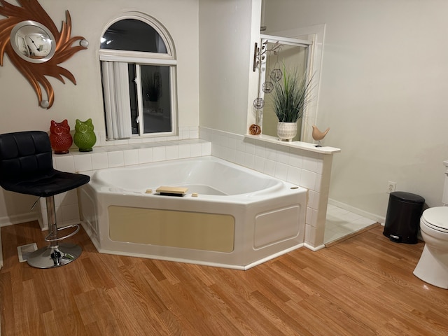 bathroom with wood-type flooring, a tub to relax in, and toilet