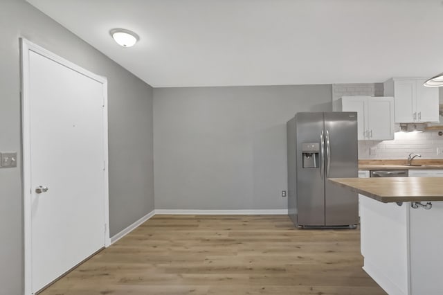 kitchen with light wood-type flooring, tasteful backsplash, stainless steel appliances, white cabinets, and butcher block countertops