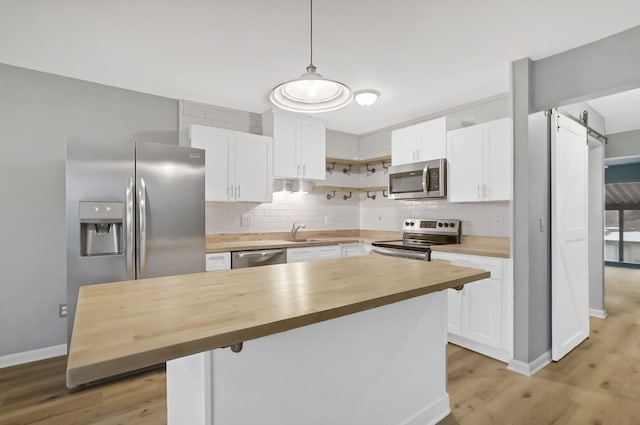 kitchen with a barn door, butcher block countertops, decorative light fixtures, white cabinetry, and stainless steel appliances