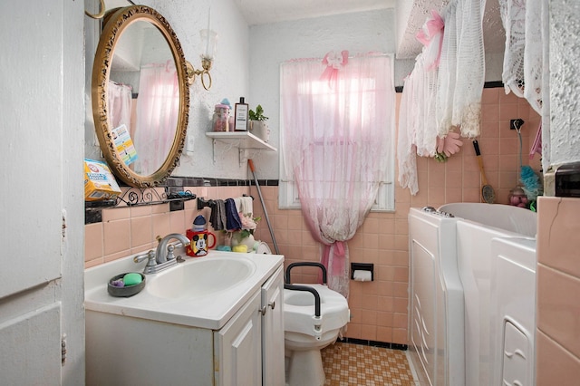 bathroom with a washtub, washer / clothes dryer, toilet, vanity, and tile walls