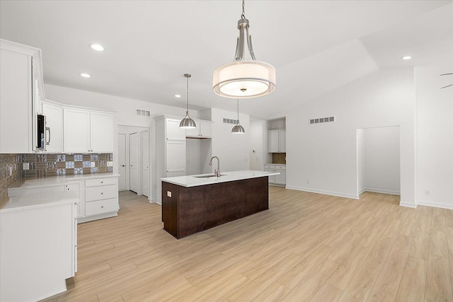 kitchen featuring white cabinetry, a kitchen island with sink, hanging light fixtures, and tasteful backsplash