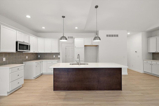 kitchen with white cabinetry, a kitchen island with sink, sink, and hanging light fixtures