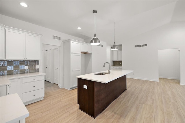 kitchen with white cabinets, backsplash, an island with sink, and sink