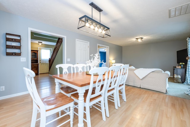 dining area featuring light hardwood / wood-style floors, a textured ceiling, and an inviting chandelier