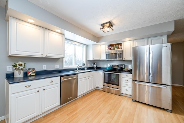 kitchen featuring white cabinetry, sink, stainless steel appliances, light hardwood / wood-style floors, and a textured ceiling