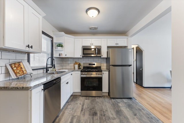 kitchen featuring sink, light stone countertops, appliances with stainless steel finishes, white cabinetry, and wood-type flooring