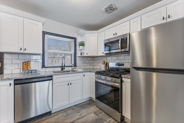 kitchen with sink, light stone counters, backsplash, white cabinets, and appliances with stainless steel finishes