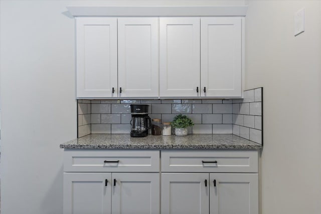 bar featuring decorative backsplash, light stone counters, and white cabinetry