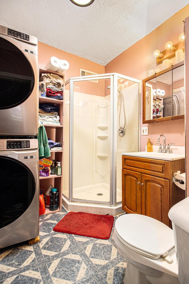 bathroom featuring vanity, a textured ceiling, stacked washer / dryer, toilet, and a shower with shower door