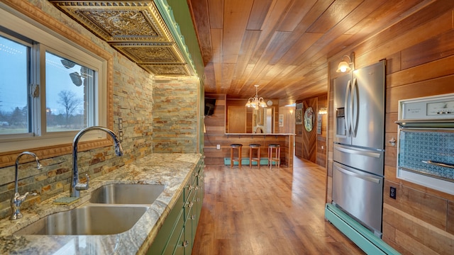 kitchen featuring sink, stainless steel fridge with ice dispenser, wooden walls, wood ceiling, and green cabinetry