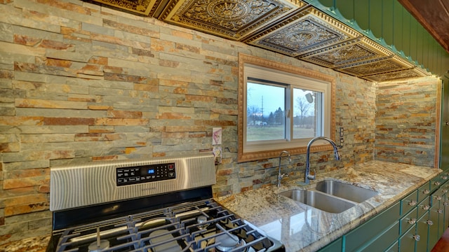 kitchen with green cabinetry, light stone counters, sink, and stainless steel range with gas stovetop