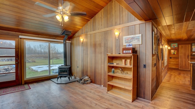 interior space featuring a wood stove, ceiling fan, wood ceiling, and vaulted ceiling