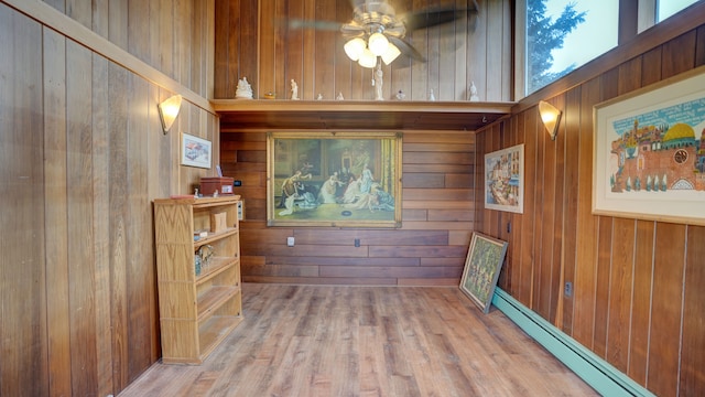 interior space featuring ceiling fan, wood walls, wood-type flooring, and a baseboard radiator