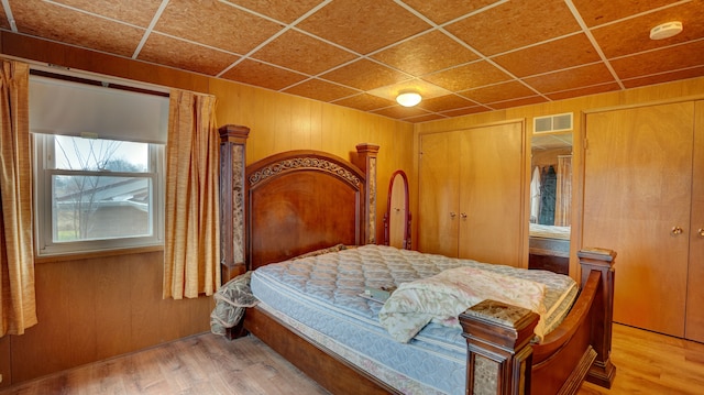 bedroom featuring a paneled ceiling, wooden walls, and light hardwood / wood-style flooring