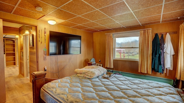 unfurnished bedroom featuring a paneled ceiling, wooden walls, and a baseboard radiator