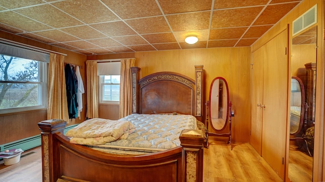 bedroom with baseboard heating, multiple windows, wooden walls, and hardwood / wood-style flooring