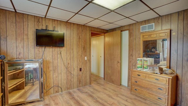 bedroom featuring light wood-type flooring, a drop ceiling, and wood walls