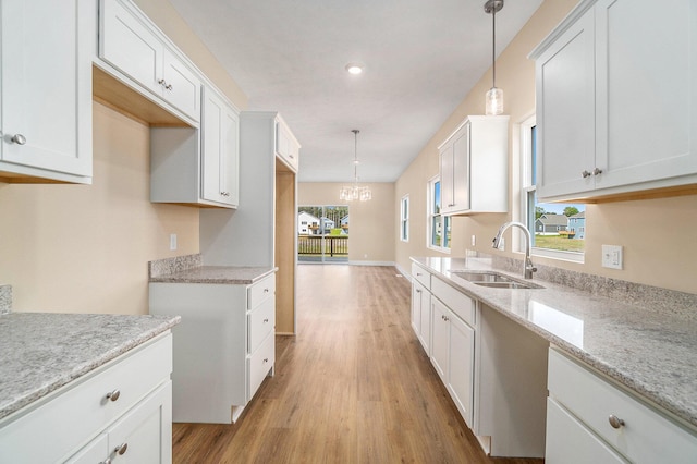 kitchen with pendant lighting, light hardwood / wood-style floors, white cabinetry, and sink