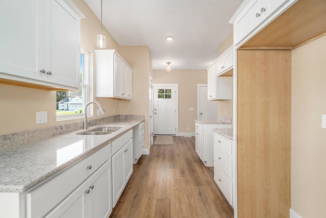 kitchen with sink, hanging light fixtures, light stone counters, light hardwood / wood-style flooring, and white cabinets