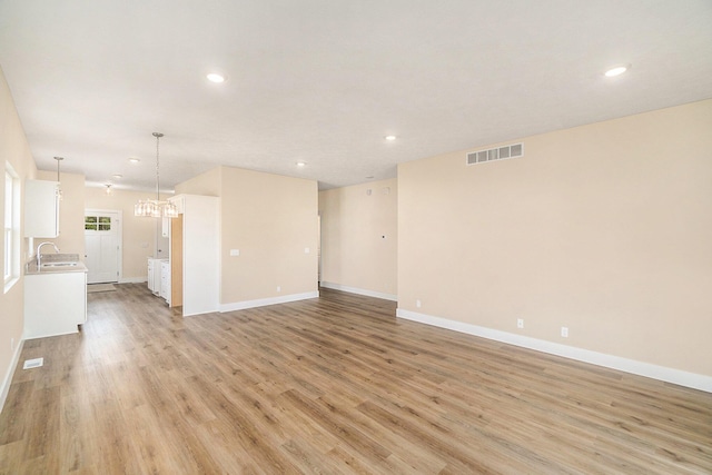 unfurnished living room featuring a chandelier, light wood-type flooring, and sink