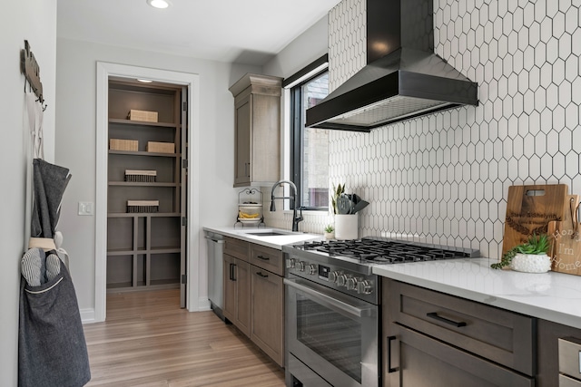 kitchen featuring sink, wall chimney range hood, light stone counters, decorative backsplash, and appliances with stainless steel finishes