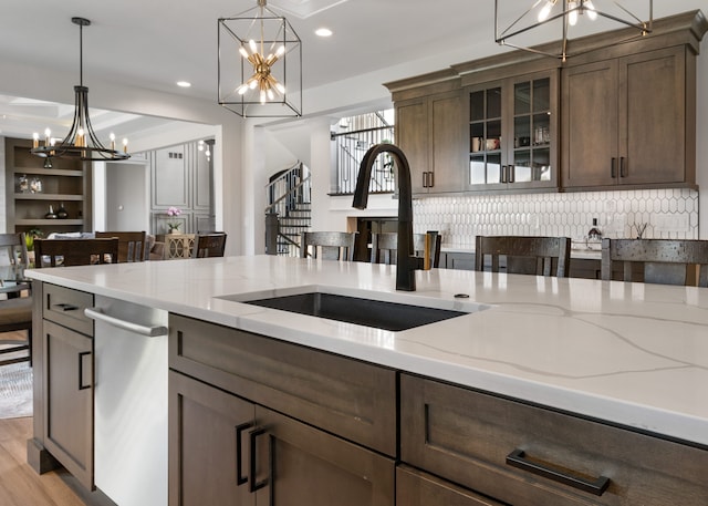 kitchen featuring sink, stainless steel dishwasher, decorative light fixtures, light hardwood / wood-style floors, and light stone counters