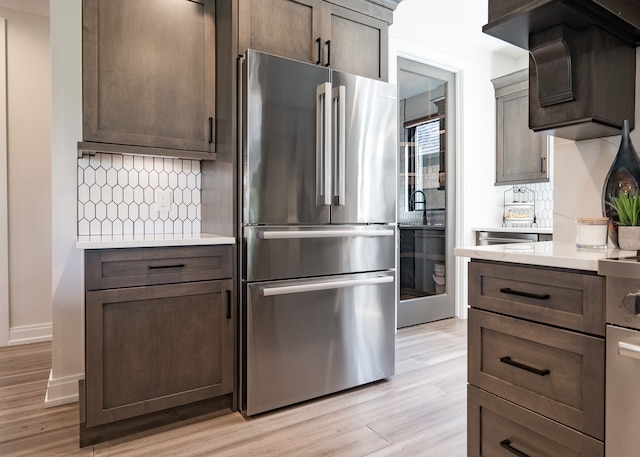 kitchen with dark brown cabinets, stainless steel fridge, decorative backsplash, and light hardwood / wood-style floors