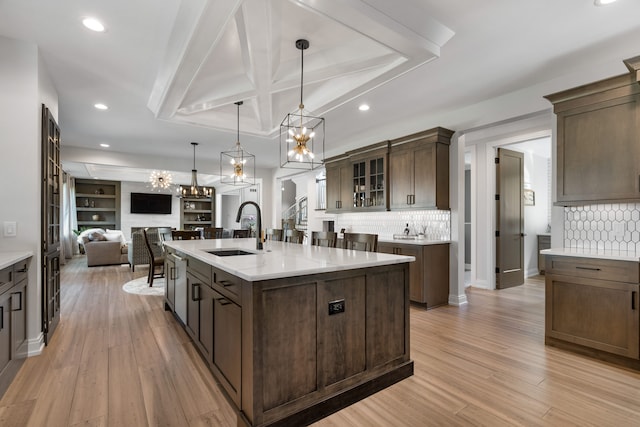 kitchen with sink, an island with sink, light hardwood / wood-style floors, decorative light fixtures, and a tray ceiling