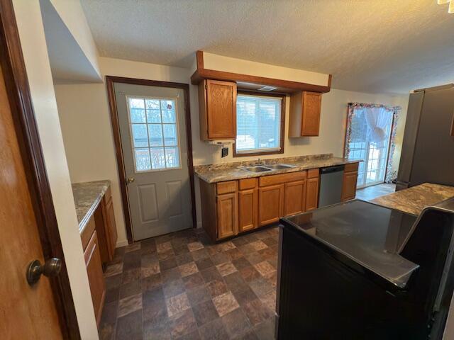 kitchen with a textured ceiling, light stone countertops, appliances with stainless steel finishes, and sink