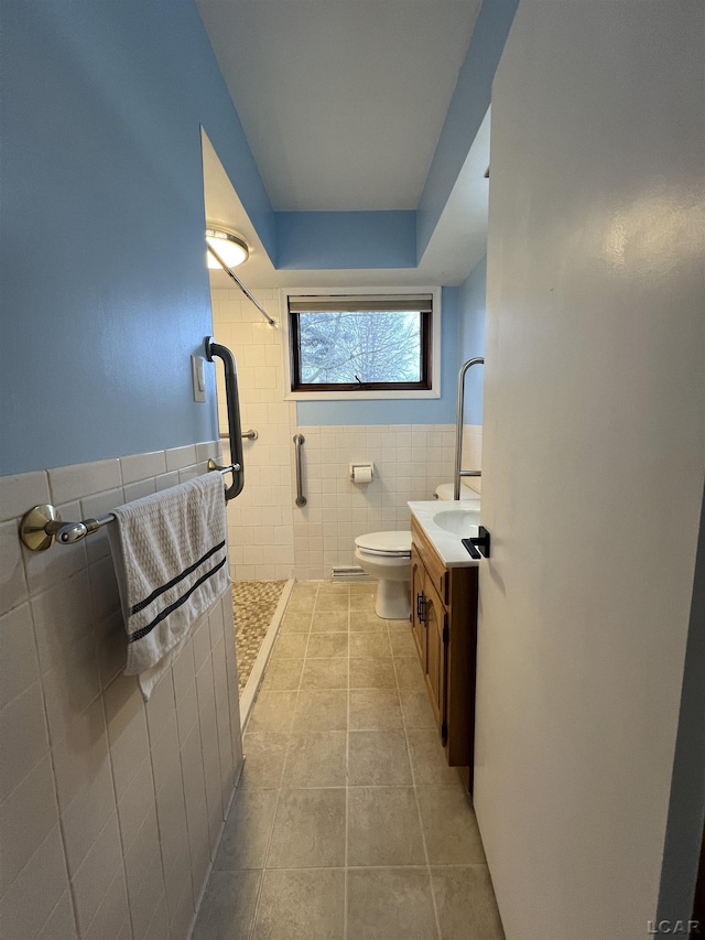 full bathroom with a wainscoted wall, toilet, a shower stall, tile patterned flooring, and tile walls