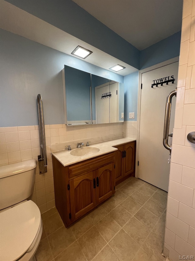bathroom with tile patterned flooring, vanity, tile walls, toilet, and wainscoting
