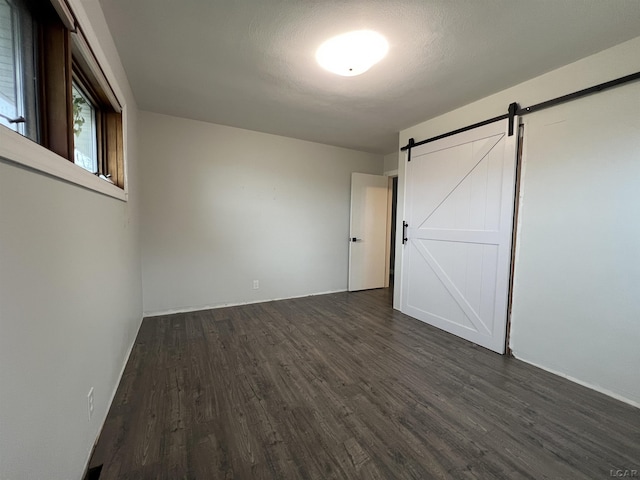 unfurnished bedroom with dark wood-type flooring and a barn door