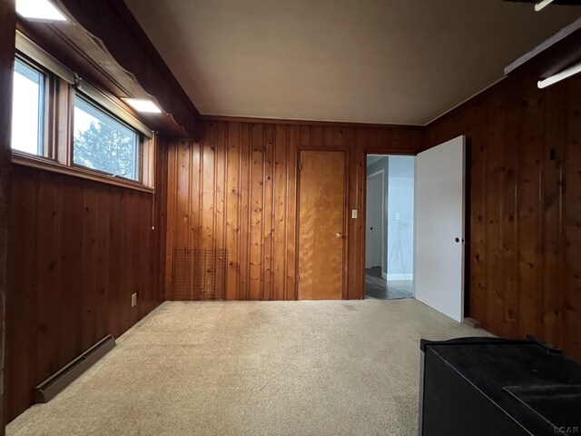 carpeted spare room with a baseboard radiator and wood walls