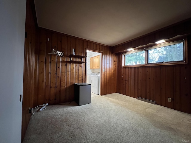 carpeted empty room with washing machine and dryer, wood walls, and baseboard heating