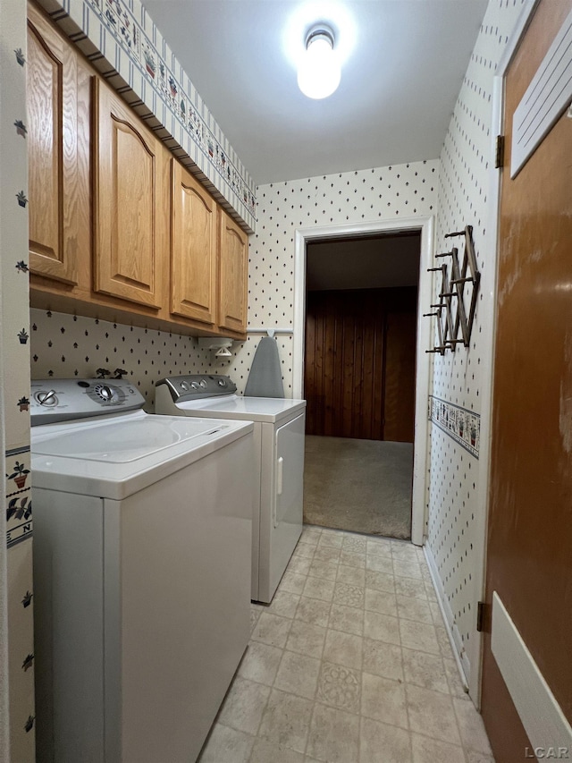 laundry room featuring washing machine and clothes dryer, cabinet space, and wallpapered walls
