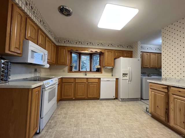 kitchen featuring a sink, washing machine and clothes dryer, brown cabinets, white appliances, and wallpapered walls