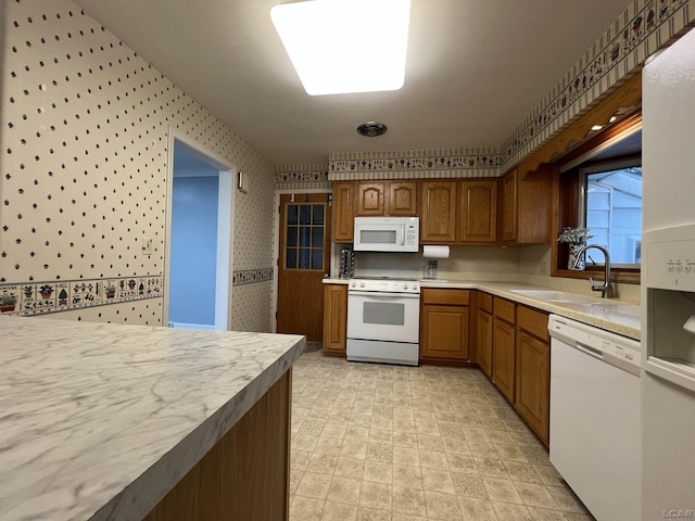 kitchen with light countertops, white appliances, wallpapered walls, a sink, and brown cabinetry
