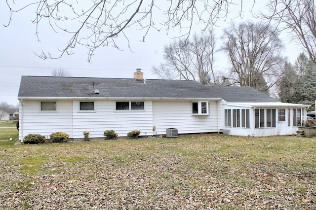 rear view of property featuring a sunroom, a chimney, central AC, roof with shingles, and a lawn