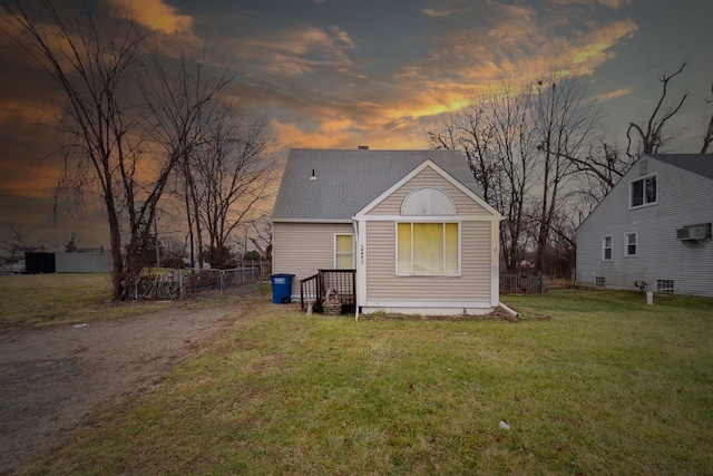 back house at dusk featuring an AC wall unit and a lawn