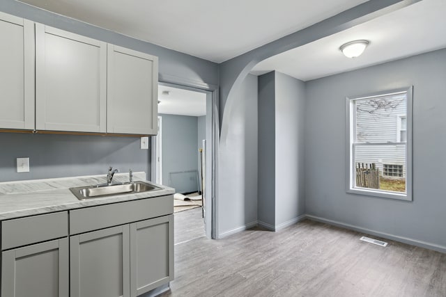 kitchen featuring gray cabinets, light stone countertops, sink, and light wood-type flooring