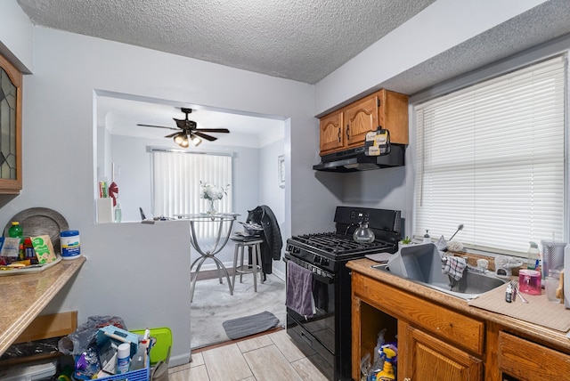 kitchen featuring under cabinet range hood, light countertops, brown cabinetry, and black gas stove