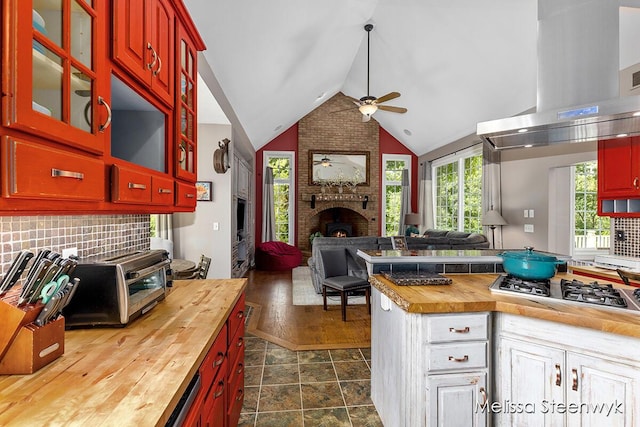 kitchen featuring stainless steel gas stovetop, a brick fireplace, ceiling fan, island range hood, and butcher block counters