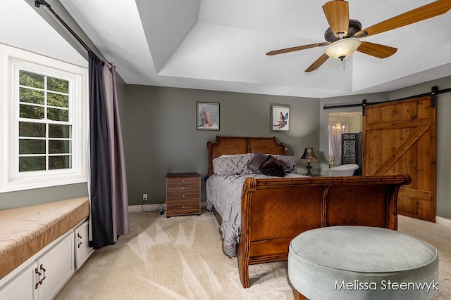 carpeted bedroom with ceiling fan, a barn door, and a tray ceiling