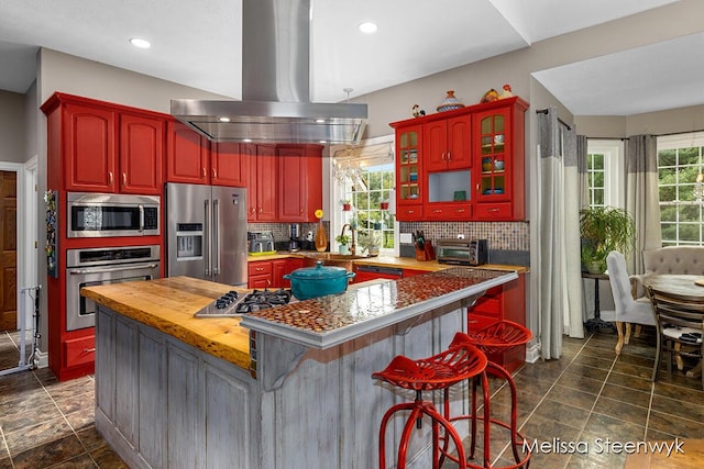 kitchen with a breakfast bar, appliances with stainless steel finishes, butcher block countertops, a kitchen island, and island exhaust hood